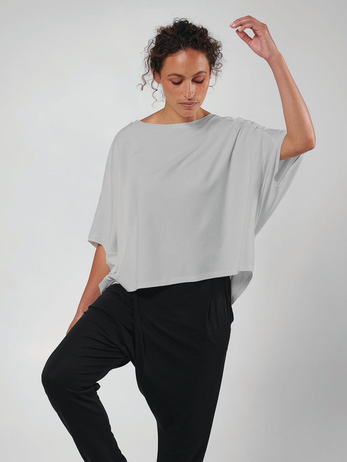 Woman wearing a light gray poncho over a black outfit on a white background.